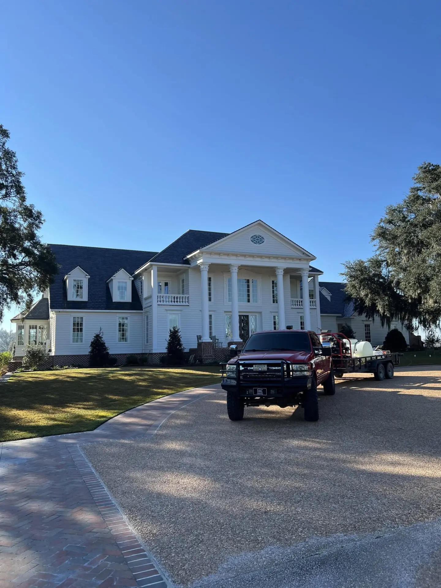 Red pressure washing truck and trailer parked in front of a large white colonial home